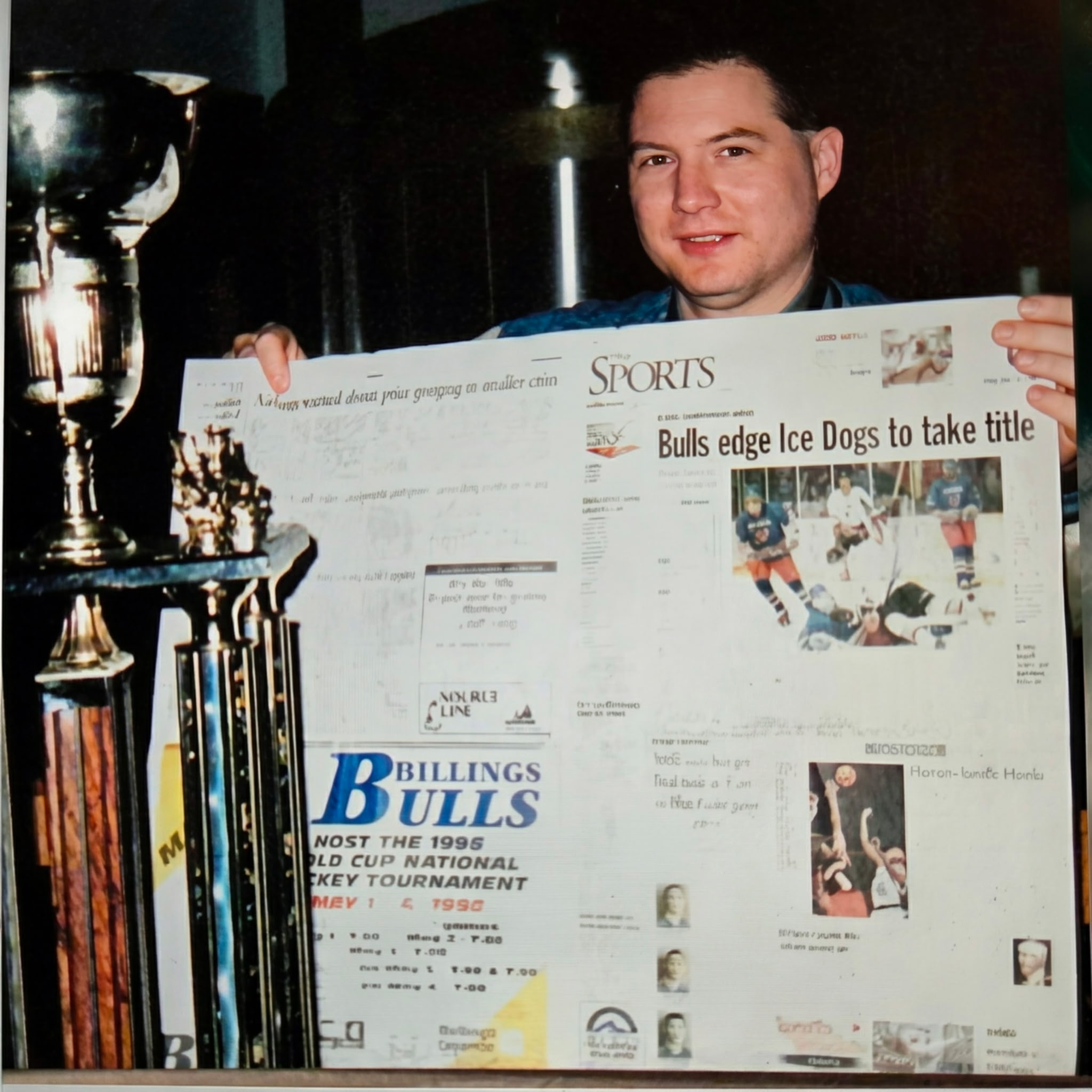 Eric Bonanno holding a Billings Bulls championship newspaper feature, with trophies beside him
